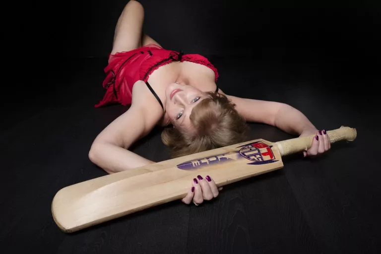 boudoir pose of a woman lying down holding a cricket bat
