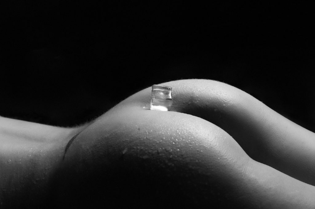black and white image of a woman's naked behind balancing an ice cube
