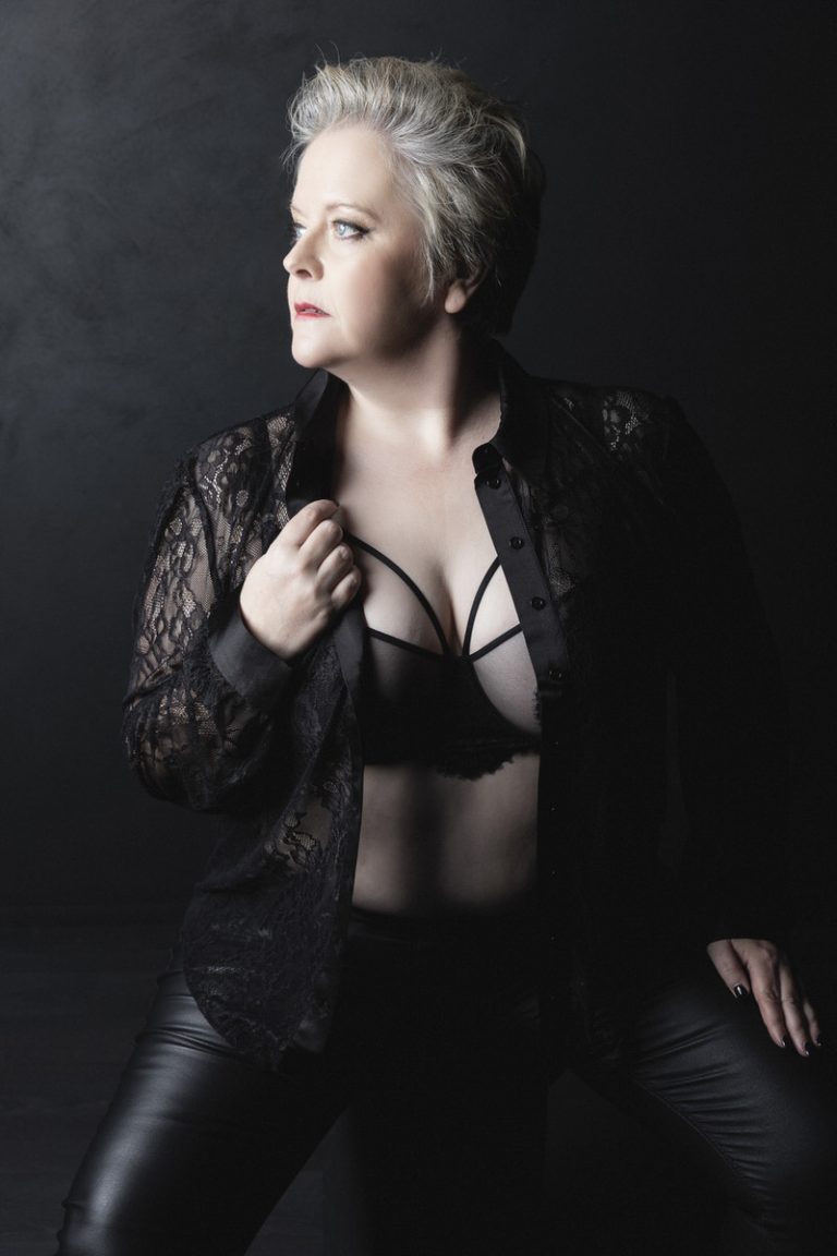 older rock chick wearing leather trousers and a black bra in a seated pose