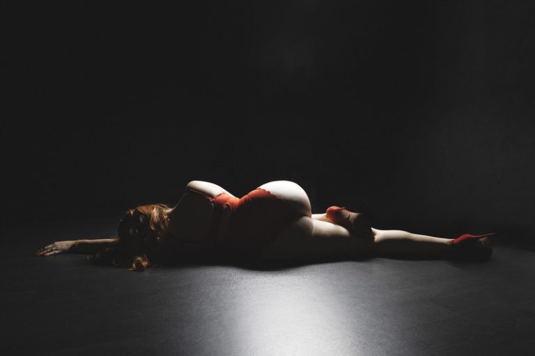 woman wearing red lacy bodysuit laying down with her back towards us