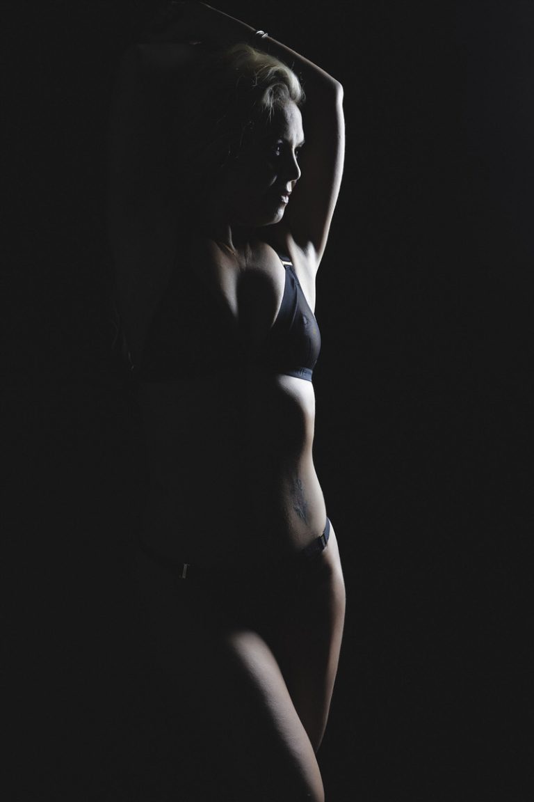 a woman wearing black bra and knickers, silhouetted agains a black wall